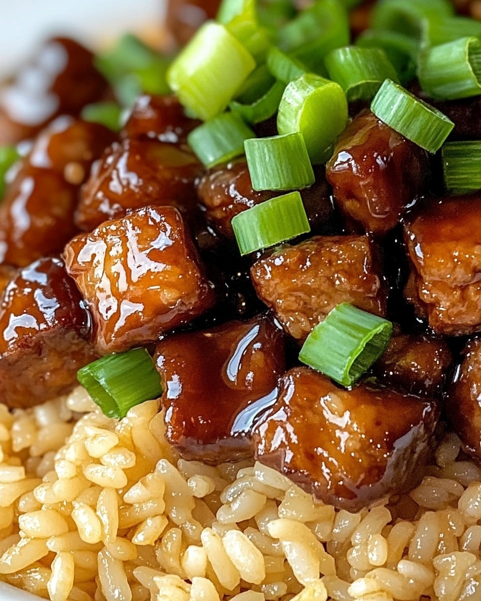 One-Pan Sweet and Tangy BBQ Sausage Rice, easy sausage and rice meal, quick dinner ideas, one-pan sausage recipes, flavorful weeknight dinners A white plate holds a single thick layer of brown fried rice mixed with small green chopped scallions spread evenly on top. Among the rice are glossy, dark brown chunks of cooked meat, glistening with sauce and scattered uniformly. The rice looks slightly oily and shiny, with the green scallions adding bright contrast. The background is a white marbled texture.