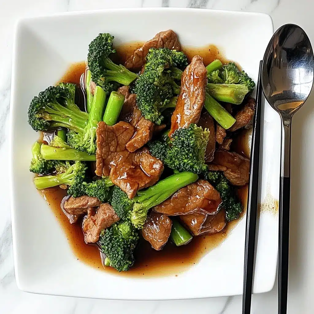 Chinese-American Beef & Broccoli, Chinese-American Beef & Broccoli recipe, easy beef and broccoli stir-fry, best beef broccoli recipe, quick Chinese beef stir-fry A white square plate holds a dish with three main layers: the first layer is a shiny, thick brown sauce spread across the plate's base; the second layer consists of bright green broccoli florets and stalks placed unevenly over the sauce; the third layer has thin, soft-looking slices of cooked brown meat arranged mixed with the broccoli. To the right side of the plate, a pair of dark brown chopsticks and a silver spoon rest, partially on the plate and the white marbled surface beneath. The