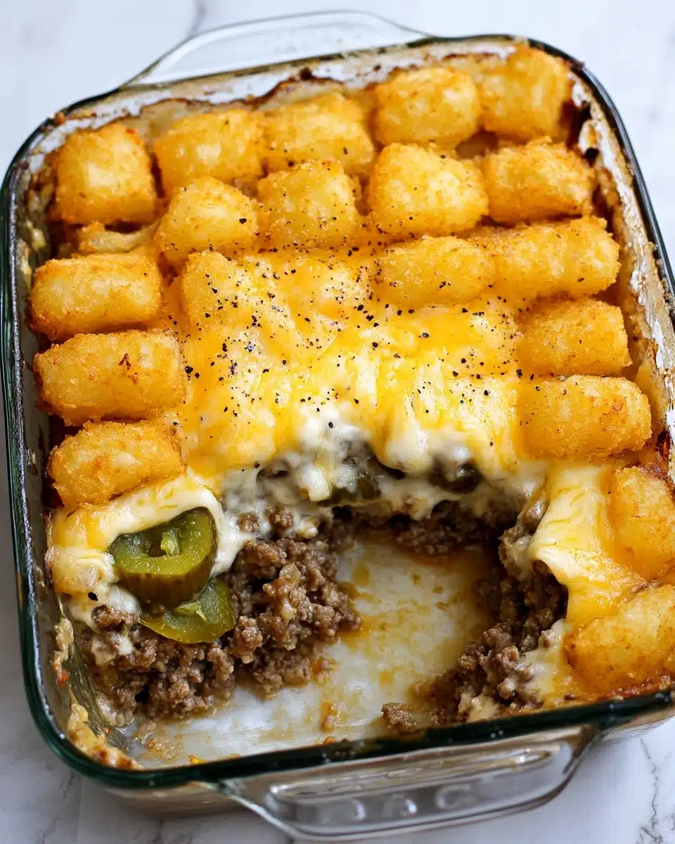 The BEST Tater Tot Casserole, delicious tater tot casserole, easy comfort food recipes, cheesy tater tot casserole, weeknight dinner ideas This dish is layered in a clear glass baking dish with four visible layers. The bottom layer is dark cooked ground meat mixed with some white sauce or dressing showing through. The second layer is green beans, chunky and bright green. The third layer is bright orange shredded cheddar cheese spread evenly. The top layer is golden-brown tater tots arranged closely together in neat rows. The dish is placed on a white marbled surface.
