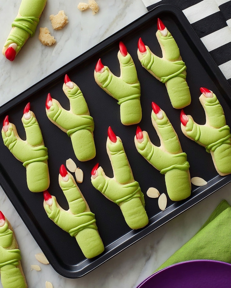 The image shows a black tray shaped like a hand holding nine green finger-shaped cookies with red tips resembling blood at the ends and red rings near the almond slice nails. Each cookie finger has three light ridge marks along its length, giving texture and a curved, finger-like look. One cookie lies outside the tray to the left, and crumbs along with a piece of cookie are on a bright green napkin to the right. The background surface is altered to a white marbled texture under a bold, black and white striped cloth. Photo taken with an iphone --ar 4:5 --v 7