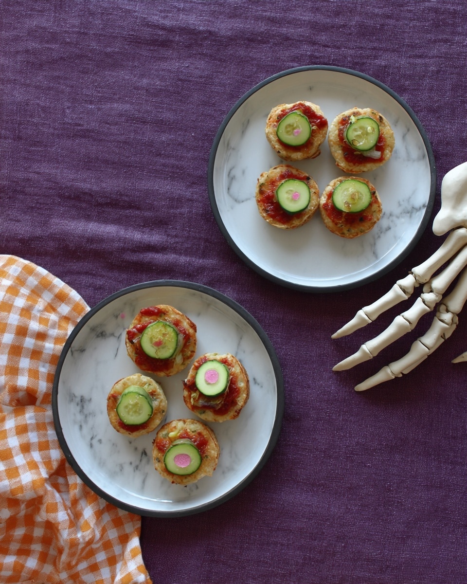 The image shows two white plates on a white marbled surface with a purple cloth underneath. Each plate holds three small round biscuit-like treats. Each treat has three layers: a soft light beige base, a thin drizzle of red sauce on top, and a slice of green cucumber with a small olive slice in the center placed on top. Two skeletal white hands are also on the surface, with one skeletal hand holding two of the treats. The scene has a playful Halloween theme with the purple cloth and skeleton decoration. Photo taken with an iphone --ar 4:5 --v 7