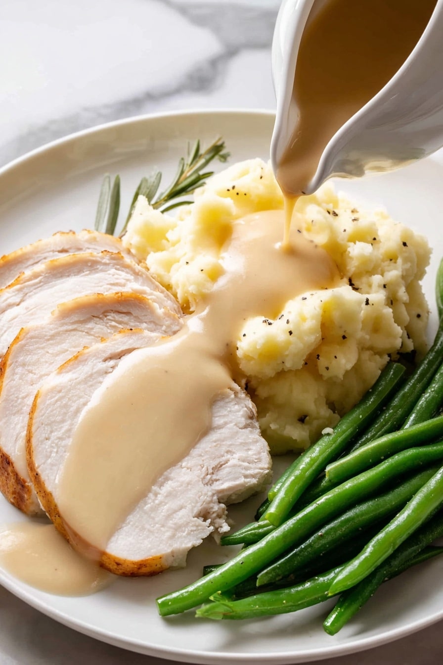 A white gravy boat filled with light brown smooth sauce, speckled with black pepper, sits on a round white speckled plate with a brown rim. Two fresh green herb sprigs, one rosemary and one sage leaf, rest beside the gravy boat on the plate. A shiny silver spoon lies on the plate next to the gravy boat, and the entire setting is placed on a white marbled surface. photo taken with an iphone --ar 2:3 --v 7 - Easy Turkey Gravy from Drippings, homemade turkey gravy, turkey gravy recipe, holiday gravy ideas, how to make turkey gravy from drippings