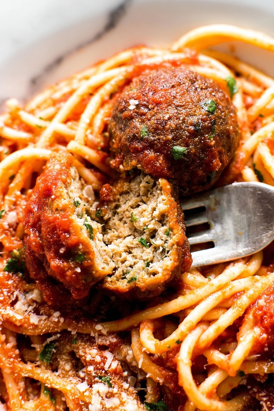 The image shows a close-up of a plate of spaghetti with tomato sauce and two meatballs, one whole and one cut in half to show its inside texture. The spaghetti is light orange with a smooth surface, coated with thick red tomato sauce that has small bits of herbs. The meatballs are brown with a slightly rough texture, and the cut meatball reveals a dense inside with green herbs mixed in. There is a sprinkling of grated cheese and chopped green herbs on top. A silver fork is placed under the cut meatball. The plate is white, and the background is a white marbled texture. photo taken with an iphone --ar 2:3 --v 7 - Spaghetti and Meatballs, Italian pasta with meatballs, Classic spaghetti and meatballs, Best homemade spaghetti and meatballs, Easy meatball recipe