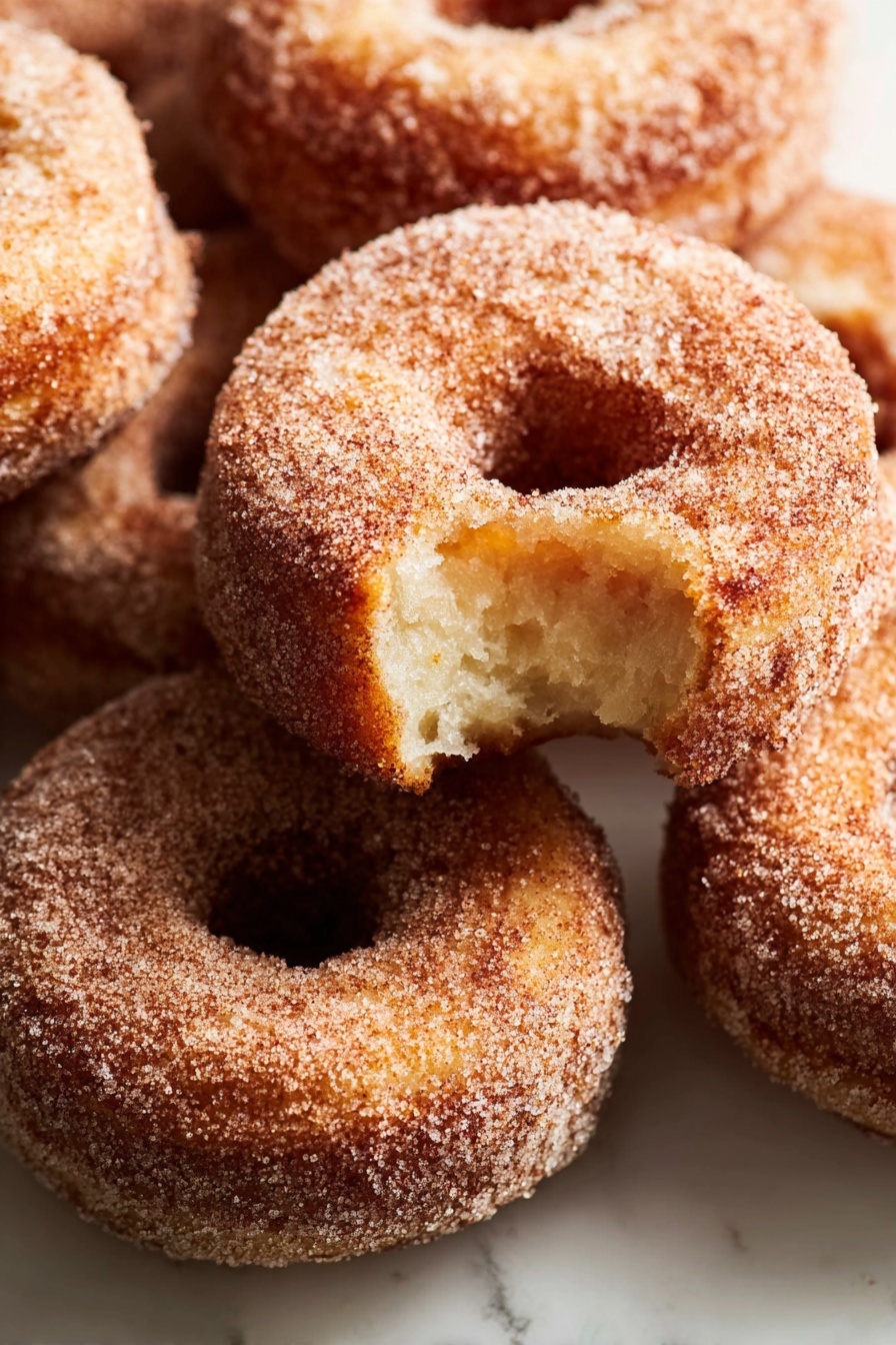 A stack of three sugar-covered donuts sits on a white marbled surface, with the top donut showing a bite taken out, revealing a soft, light brown inside. Each donut has a rough texture coated evenly in sugar, giving a slightly grainy look. The donuts are arranged one on top of the other, with the bitten one on the top, the middle and bottom donuts fully intact, all round with a visible center hole. The lighting softly highlights the sugar crystals and the golden brown color of the fried dough. photo taken with an iphone --ar 2:3 --v 7 - Apple Cider Donuts, Apple Cider Donuts Recipe, Fall Donut Recipes, Cinnamon Sugar Donuts, Homemade Apple Cider Donuts