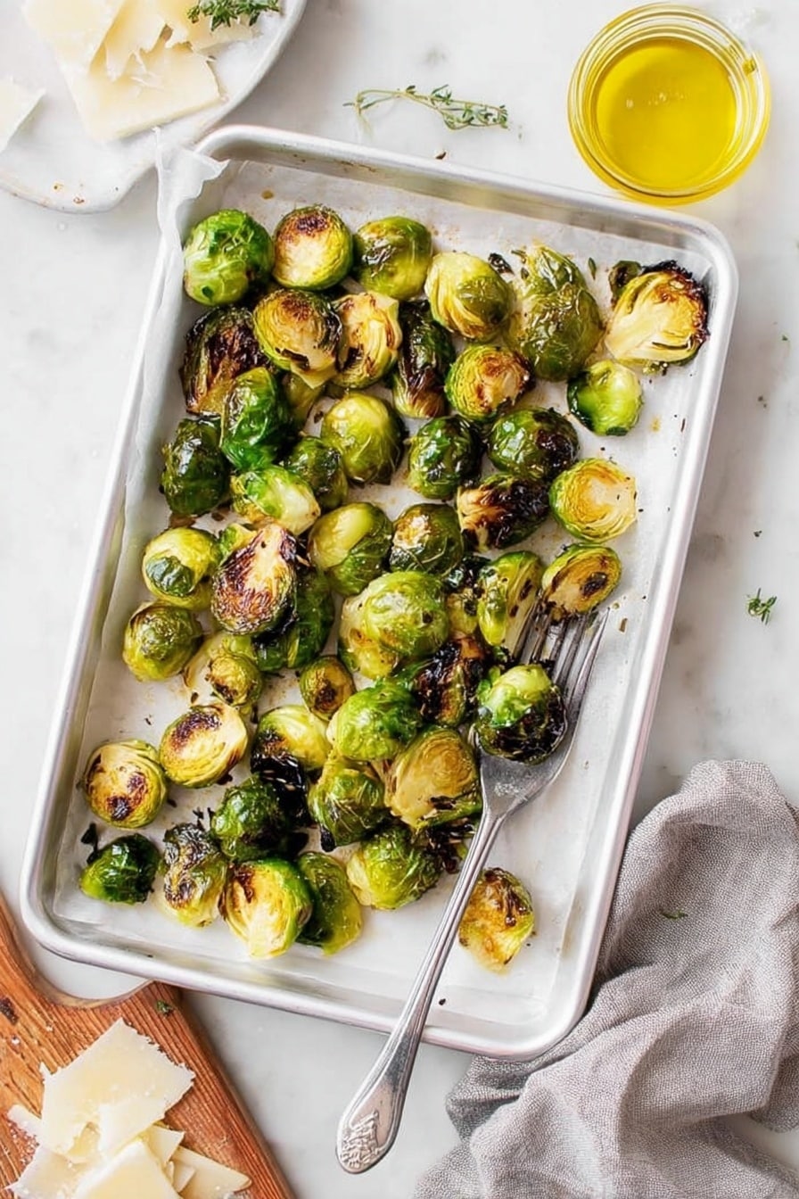 A white baking tray lined with white parchment paper holds a single layer of roasted Brussels sprouts, some halved and some whole, showing a mix of bright green and dark brown charred spots, giving a crispy texture. The tray is placed on a white marbled surface with a silver fork resting in the bottom right corner inside the tray. To the right, there is a small glass jar filled with yellow oil, and at the bottom left corner, part of a wooden board with thinly shaved white cheese is visible, along with a grey cloth nearby. The overall scene is bright and fresh, highlighting the crispy roasted Brussels sprouts. photo taken with an iphone --ar 2:3 --v 7 - Lemon Parmesan Roasted Brussels Sprouts, Brussels Sprouts Side Dish, Easy Vegetable Recipes, Healthy Spring Sides, Crispy Roasted Brussels Sprouts