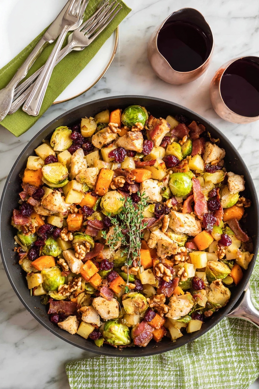 A large black pan filled with a colorful mix of cooked ingredients sits on a white marbled surface with a green cloth and fork on the left. The mix has three main layers: a base of cubed orange sweet potatoes, light yellow apple pieces, and halved green Brussels sprouts; a middle layer of beige chicken pieces and crispy, dark brown bacon bits; and a top layer of whole walnuts and dried dark red cranberries. A small sprig of fresh green thyme rests on top, and a wooden spoon leans inside the pan from the right side. Two glasses filled with dark red wine are placed nearby on the white marbled surface, with one glass partially reflected on a shiny black bowl. photo taken with an iphone --ar 2:3 --v 7 - One-Pot Easy Harvest Chicken Skillet, autumn chicken skillet, quick chicken dinner, cozy fall recipes, one-pan chicken meal