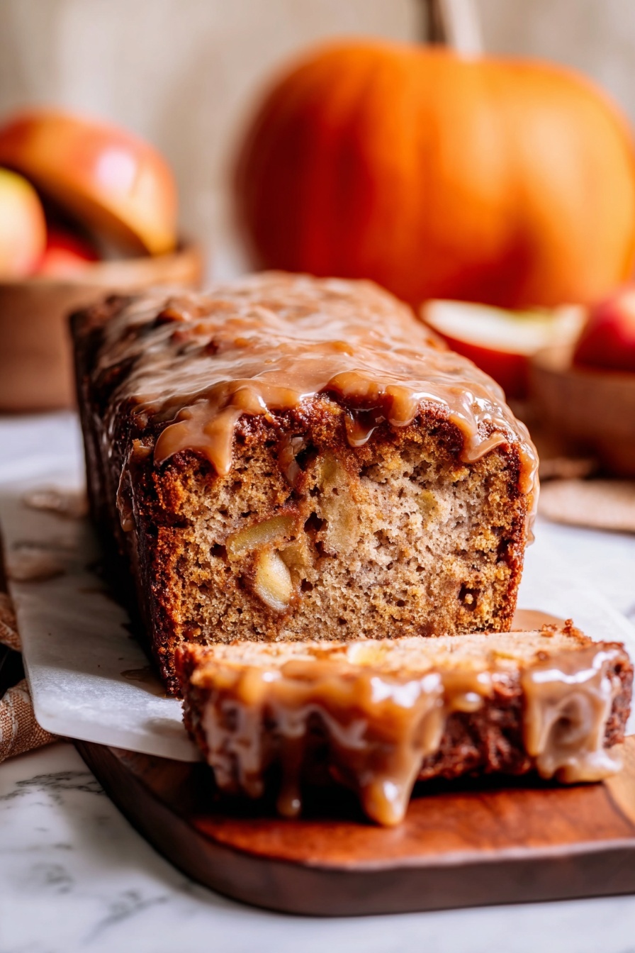 A loaf cake sits on a wooden board over a white marbled surface, sliced at the front showing its dense, light brown inside with visible chunks of apple. The top layer is a thick, sticky, darker brown glaze that drips down the sides, giving the cake a shiny look. In the background, there is a small orange pumpkin and a wooden bowl with apples that add warm tones to the image. The photo is warm and cozy, focusing tightly on the textures of the cake and glaze, with a soft, light blur in the background. photo taken with an iphone --ar 2:3 --v 7 - Amish Apple Fritter Bread, apple fritter bread recipe, cinnamon apple quick bread, easy apple bread with glaze, moist apple cinnamon bread