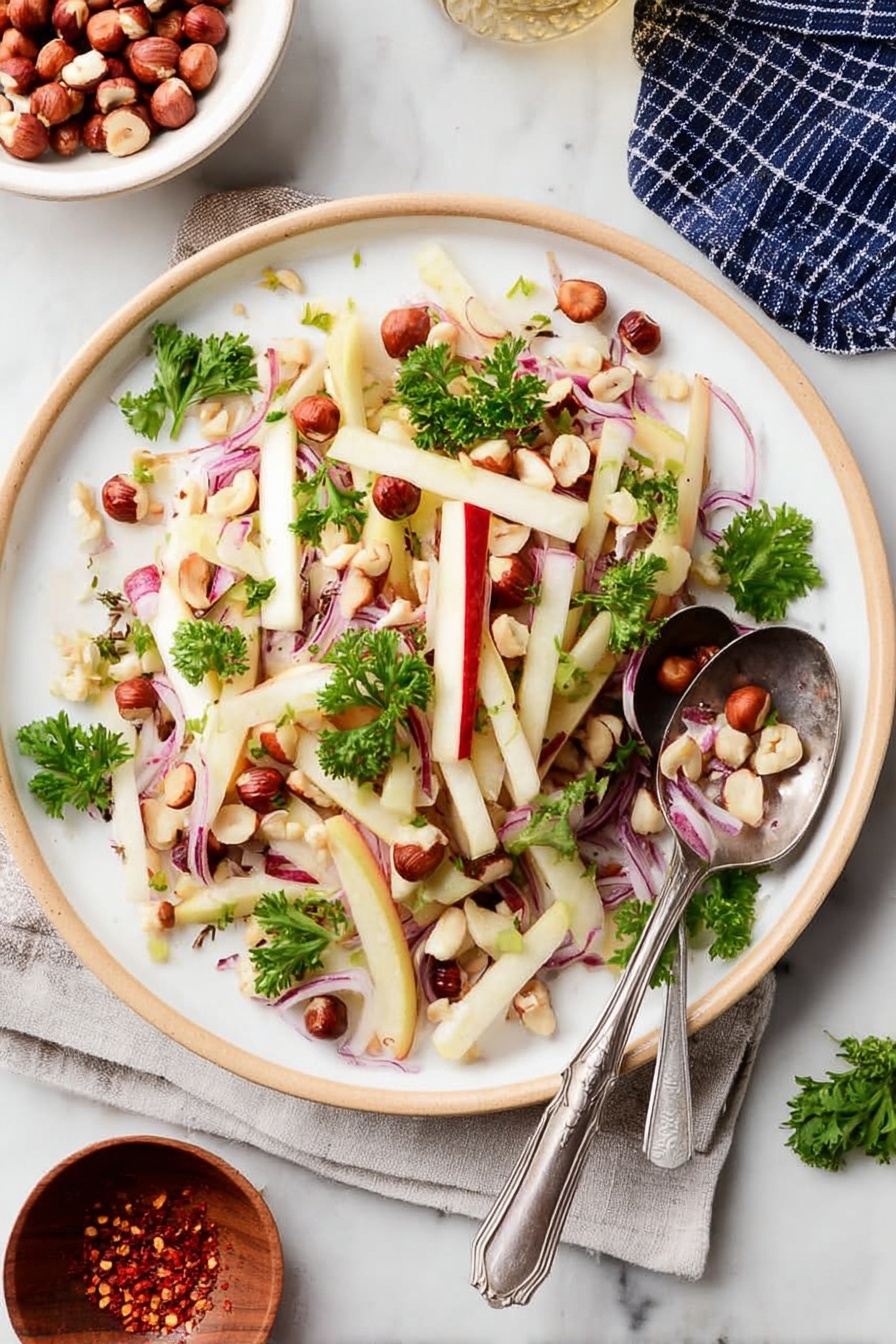 The image shows a white plate filled with a fresh salad consisting of thin, pale yellow sticks of apple with red skin edges, thin slices of purple-red onion bent softly, and scattered small whole brown hazelnuts along with some halved ones. Bright green parsley leaves are sprinkled on top, adding color contrast. A silver spoon and fork rest on the right side of the plate, partly on the salad. The plate is set on a white marbled surface. photo taken with an iphone --ar 2:3 --v 7 - Kohlrabi Slaw with Apples and Hazelnuts, healthy kohlrabi salad, crunchy apple slaw, toasted hazelnut salad, easy vegetable slaw