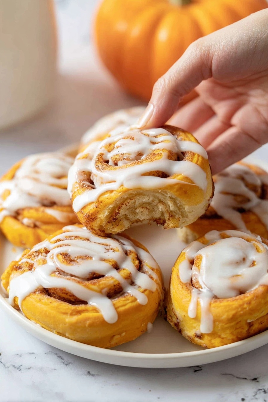 A white plate filled with six bright orange spiral rolls, each topped with a thick drizzle of white icing. The rolls have multiple visible layers with a soft, doughy texture and a cinnamon-spice swirl inside that adds a speckled light brown pattern. A woman's hand is gently lifting one roll from the plate, showing more of its smooth icing on the top center. The background is a white marbled texture with a small orange pumpkin blurred in the back. photo taken with an iphone --ar 2:3 --v 7 - Pumpkin Cinnamon Rolls with Cream Cheese Glaze, pumpkin cinnamon rolls, fall cinnamon roll recipes, pumpkin dessert ideas, easy cinnamon roll recipes