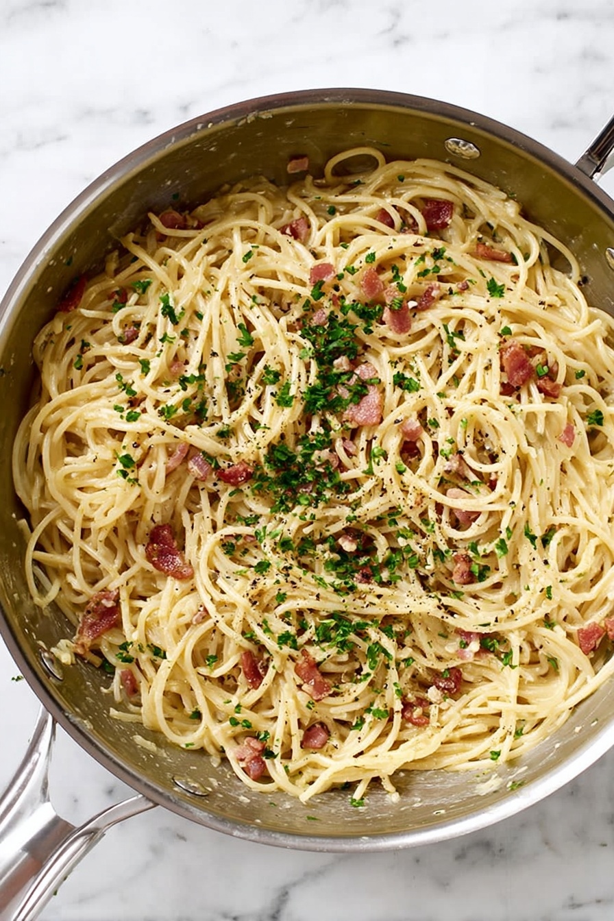 A silver metal pan filled with spaghetti noodles mixed with small pieces of reddish-brown bacon and finely chopped green parsley sprinkled on top. The pasta has a light cream sauce coating, and tiny black pepper bits are scattered throughout. The pan is placed on a white marbled surface. Photo taken with an iphone --ar 2:3 --v 7 - Spaghetti Carbonara, quick Italian pasta, creamy pasta without cream, easy weeknight dinner, classic Italian dish