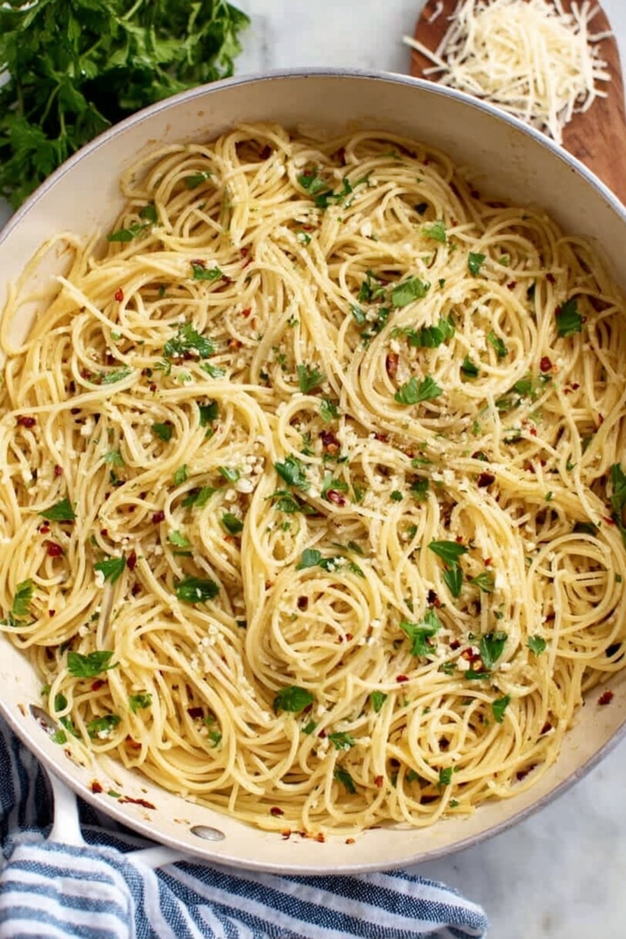 A white pan filled with a single layer of thin spaghetti pasta cooked and mixed with small bits of white garlic and red chili flakes spread throughout. Fresh green parsley leaves are scattered on top, adding a touch of color and freshness. The pan rests on a white marbled surface next to a blue and white striped cloth, with fresh parsley and some shredded cheese partially visible in the background. Photo taken with an iphone --ar 2:3 --v 7 - Garlic Olive Oil Spaghetti, garlic pasta recipe, easy garlic pasta, quick Italian pasta, comforting garlic spaghetti