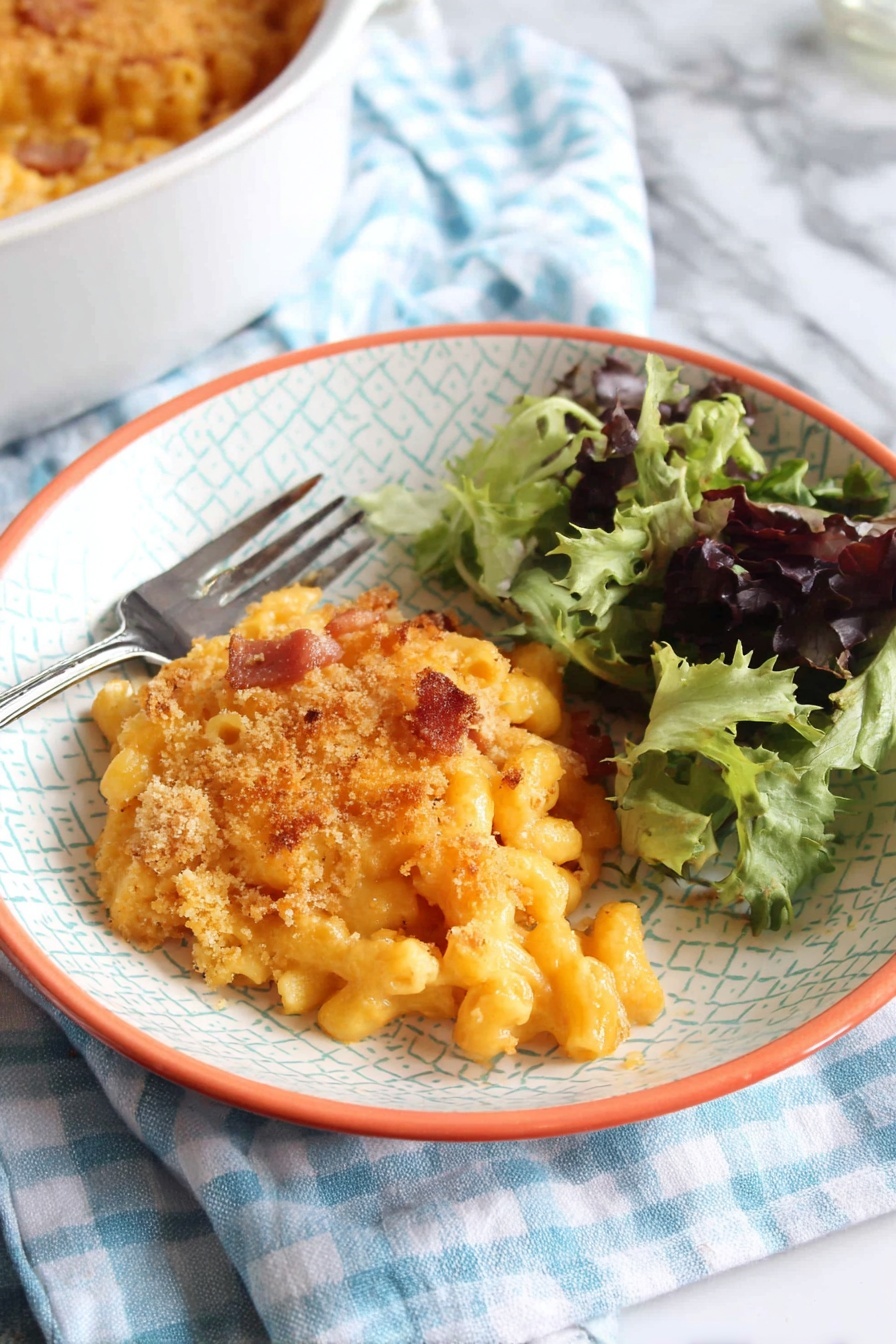 A white bowl with a light geometric pattern and orange rim holds a serving of baked macaroni and cheese topped with a golden breadcrumb crust with some browned spots. The macaroni pasta under the crust is creamy and orange, with small pieces of browned bacon or ham mixed inside. To the right side of the bowl is a small fresh salad of mixed green leaves, some dark purple and others bright green with curly texture. A silver fork rests on the left edge of the bowl. The bowl sits on a blue and white checkered cloth over a white marbled surface. In the bottom left corner, part of a white round baking dish filled with more macaroni and cheese is visible. photo taken with an iphone --ar 2:3 --v 7 - Chorizo Mac and Cheese Bake, spicy mac and cheese recipe, creamy cheese and chorizo casserole, easy comfort food recipes, smoky chorizo pasta bake