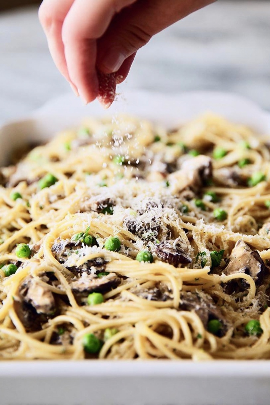 A round serving of baked pasta with visible noodles, small green peas, and bits of light beige chicken arranged in the center of a shiny white plate with a blue rim. The top layer is sprinkled with golden toasted breadcrumbs, adding a rough texture. A silver fork is placed on the right side of the plate, its tines partly under the pasta. The plate rests on a white marbled surface, and in the blurry background, there is a white baking dish filled with more of the same pasta bake. The light is soft and natural, showing the creamy and slightly browned surface of the pasta. photo taken with an iphone --ar 2:3 --v 7 - Turkey Mushroom Pasta Bake, comforting pasta casserole, easy turkey pasta bake, creamy mushroom pasta, hearty family dinner