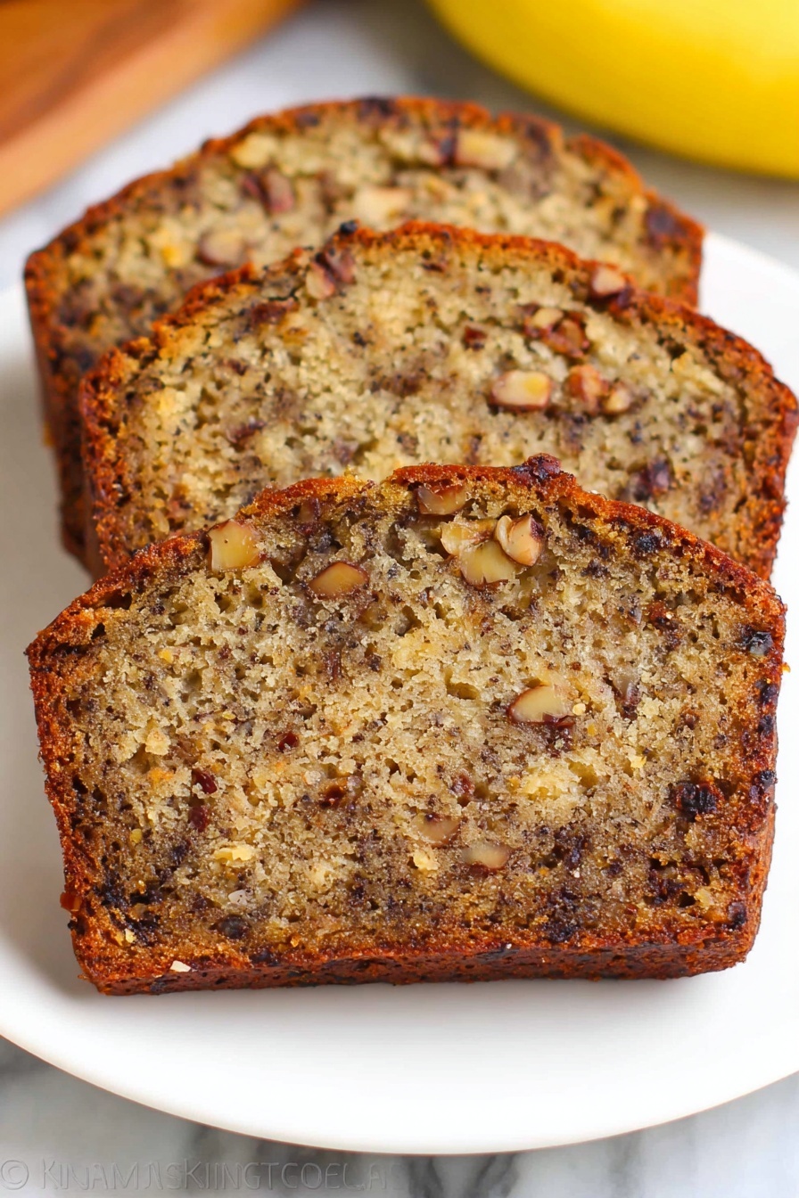 Three slices of banana nut bread are stacked slightly overlapping on a white plate, showing a dense texture filled with dark brown nuts and small chunks of banana inside the golden brown cake. The crust is a darker shade of brown and slightly crisp, while the inside looks moist with a mix of light and dark brown colors from the bananas and nuts. The plate is on a white marbled surface with a blurred yellow banana visible in the background. Photo taken with an iphone --ar 2:3 --v 7 - Best Moist Banana Bread with Walnuts, moist banana bread recipe, easy banana bread with walnuts, tender banana bread, homemade banana bread
