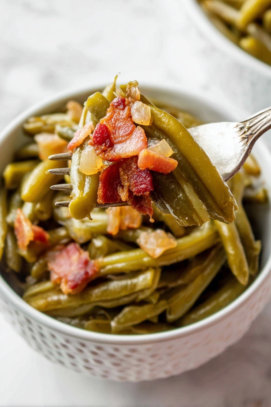 A white bowl with a pattern holds cooked green beans layered at the bottom, soft and shiny with a slightly wrinkled texture. On top, small chunky pieces of browned bacon with a reddish-brown tone and a bit of translucent cooked onion are mixed in. A fork lifts some green beans and bacon from the bowl, showing the layers clearly, with the vegetables still moist and the bacon crispy in places. The background is a white marbled surface. photo taken with an iphone --ar 2:3 --v 7 - Crock Pot Green Beans with Bacon, green beans with bacon, easy green bean side dish, slow cooker green beans, bacon green bean recipe