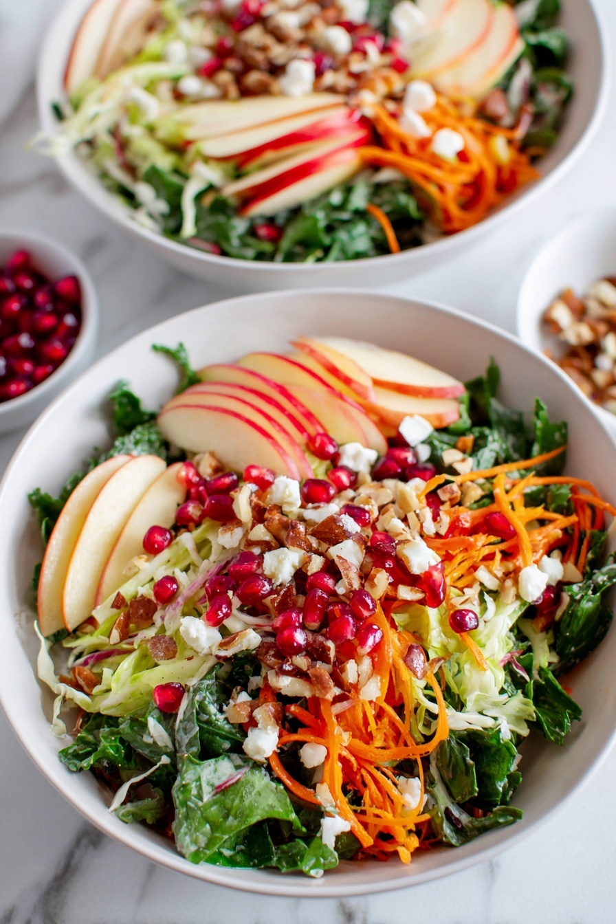 The image shows two white bowls on a white marbled surface, each filled with a colorful salad made of multiple layers. The base layer includes bright dark green leafy vegetables, rich orange shredded carrots, and pale green shredded cabbage. On top of this, there are thin slices of red and yellow apples arranged spread out, bright red pomegranate seeds scattered evenly, and small pieces of crumbled white cheese. There are also light brown chopped nuts sprinkled throughout, adding texture. The salad appears fresh and vibrant, with a mix of rough and smooth textures. Photo taken with an iphone --ar 2:3 --v 7 - Winter Kale Salad with Apples and Pomegranate, healthy winter salad, kale and pomegranate salad, apple winter salad, vibrant winter greens