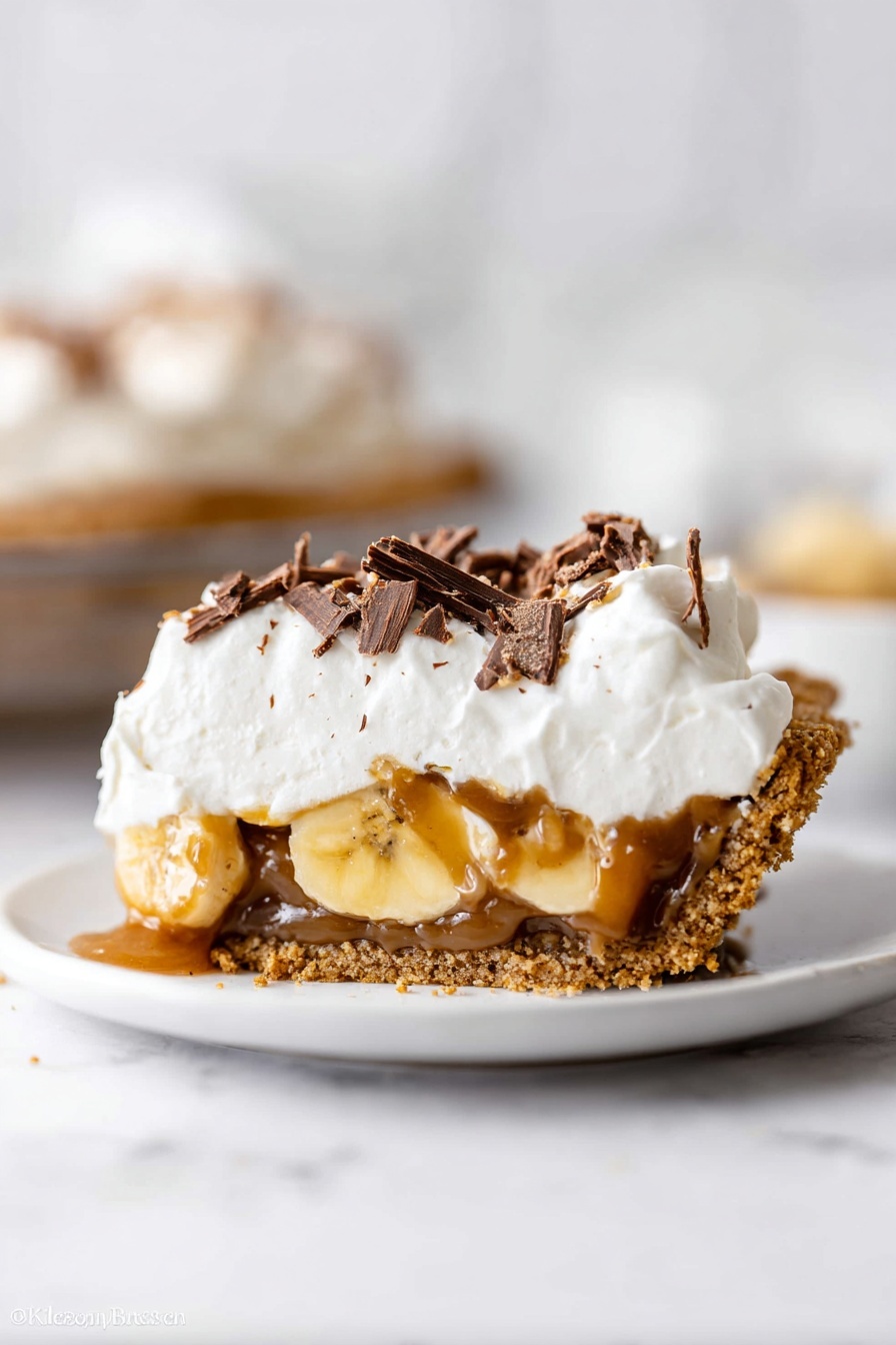 This image shows a close-up of a pie in a clear glass dish on a white marbled surface. The pie has four visible layers: a base layer of golden brown crumbly crust, a layer of light brown caramel filling, a thick layer of sliced pale yellow bananas, and a top layer of fluffy white whipped cream. The whipped cream is decorated with thin dark brown chocolate shavings scattered on top. Part of the pie is missing, revealing the inside layers clearly. The photo taken with an iphone --ar 2:3 --v 7 - Decadent Banoffee Pie with Dulce de Leche, Banoffee Pie with Dulce de Leche, easy banoffee pie recipe, homemade banoffee dessert, creamy caramel banana pie