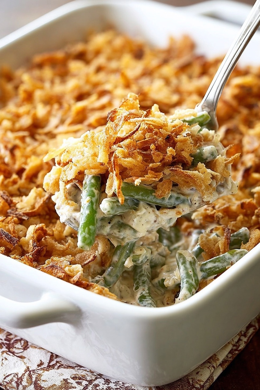 A white rectangular baking dish filled with a creamy green bean casserole topped with a thick layer of crispy golden brown fried onions. The casserole shows soft green beans mixed with a light beige creamy sauce beneath the crunchy topping. In the foreground, a white spoon lifts a serving, revealing the creamy texture mixed with green beans and bits of fried onions. The dish is placed on a table with a white marbled texture showing under the edges. Photo taken with an iphone --ar 2:3 --v 7 - Green Bean Casserole with Bacon and Mushrooms, green bean casserole recipe, bacon mushroom side dish, easy green bean casserole, comfort food casseroles