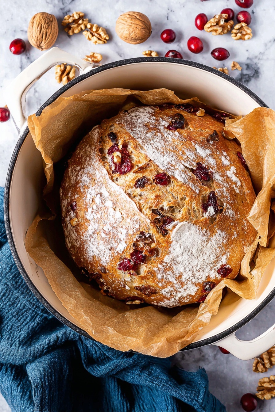 A close-up image shows two thick slices of bread placed on a wooden board against a white marbled texture background. The bread has a golden-brown crust and a light beige inside filled with visible pieces of red cranberries and light brown walnuts spread evenly throughout. The texture looks soft with small holes in the crumb. In the top left corner of the image, there are some walnut pieces and dried cranberries scattered on the wooden board. A dark gray cloth is also partly visible in the upper right area. photo taken with an iphone --ar 2:3 --v 7 - No-Knead Cranberry Walnut Bread, cranberry walnut bread, holiday bread recipes, easy homemade bread, festive bread with cranberries and walnuts