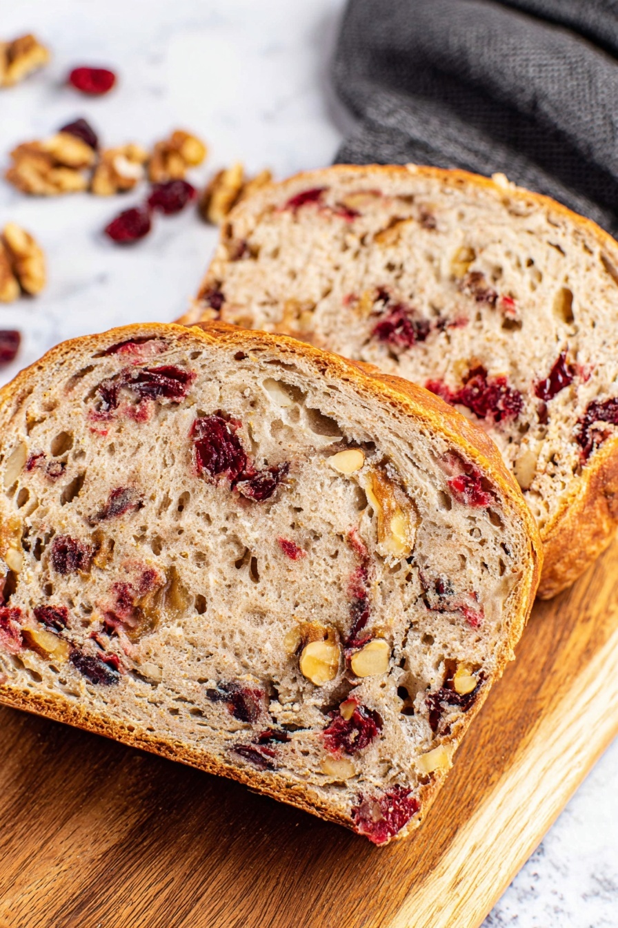 A round loaf of bread with a golden brown crust dusted with white flour is placed in a white pot lined with parchment paper. Visible inside the crust are pieces of red cranberries and light brown walnuts, adding texture and color contrast. Around the pot on the white marbled surface, whole walnuts and scattered dried cranberries create a natural decoration. A dark blue cloth rests partially under the pot’s handle, adding a soft touch to the scene. The overall look shows a rustic, fresh bread with a mix of crunchy and chewy textures photo taken with an iphone --ar 2:3 --v 7 - No-Knead Cranberry Walnut Bread, cranberry walnut bread, holiday bread recipes, easy homemade bread, festive bread with cranberries and walnuts