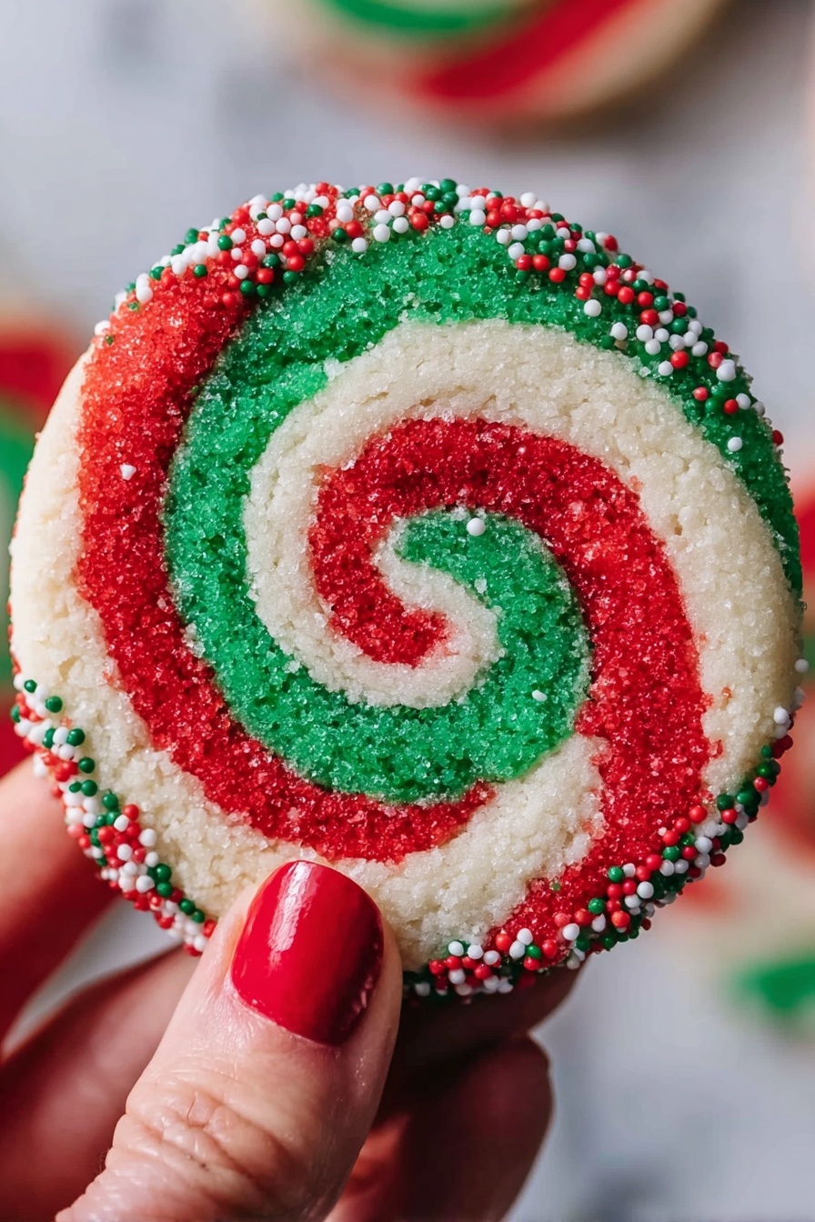A round cookie with a red, white, and green swirl pattern that forms a spiral from the center to the edges. The outer edge of the cookie is coated with small red, white, and green round sprinkles. A woman's hand with red nail polish holds the cookie against a blurred background, and the surface under the cookie is white marbled texture. photo taken with an iphone --ar 2:3 --v 7 - Colorful Swirled Christmas Cookies, festive holiday cookies, colorful holiday cookies, Christmas cookie ideas, vibrant Christmas treats
