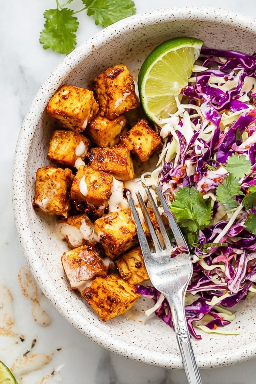 The image shows a white speckled bowl with two main layers: on one side, there are small, golden-brown seasoned cubes with a smooth light sauce drizzled over them, and on the other side, there is a mix of shredded purple and white cabbage with some green cilantro leaves scattered on top. A wedge of bright green lime sits at the edge of the bowl. A silver fork is placed inside, resting on the bowl’s edge and touching some of the cubes. The bowl is on a white marbled surface with some sauce drops visible nearby. Photo taken with an iphone --ar 2:3 --v 7 - Fish Taco Bowl with Spicy Mayo, fish taco bowl, spicy mayo fish bowl, quick fish taco dinner, healthy fish taco recipe