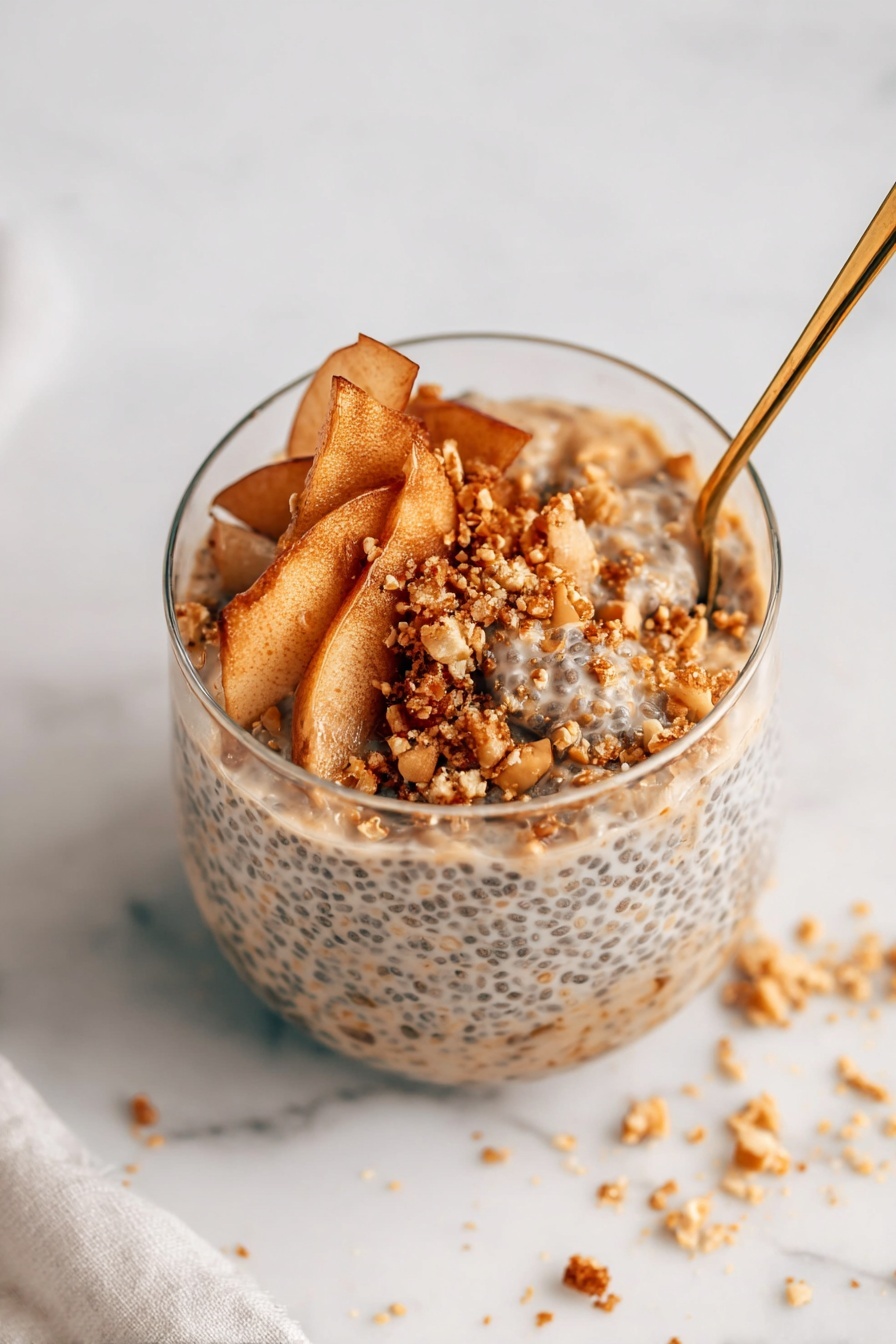 A clear glass filled with three main layers is shown on a white marbled surface. The bottom layer is a thick, creamy mixture with visible small black chia seeds evenly distributed, giving it a speckled texture. On top of that, there is a layer of thin, light brown apple slices with a soft texture, slightly curled and overlapping in a loose arrangement. The top layer is sprinkled with small, coarse granules of golden brown crumbs and chopped nuts, adding a crunchy texture and contrasting color. A gold spoon is inserted on the right side of the glass, partly immersed in the layers. Some crumbs are scattered around on the white marbled surface near the glass, showing slight messiness. photo taken with an iphone --ar 2:3 --v 7 - Apple Cinnamon Chia Pudding with Fruit Crumble, healthy apple cinnamon breakfast, nutritious chia pudding with fruit topping, cozy fall breakfast recipes, easy fruit crumble dessert