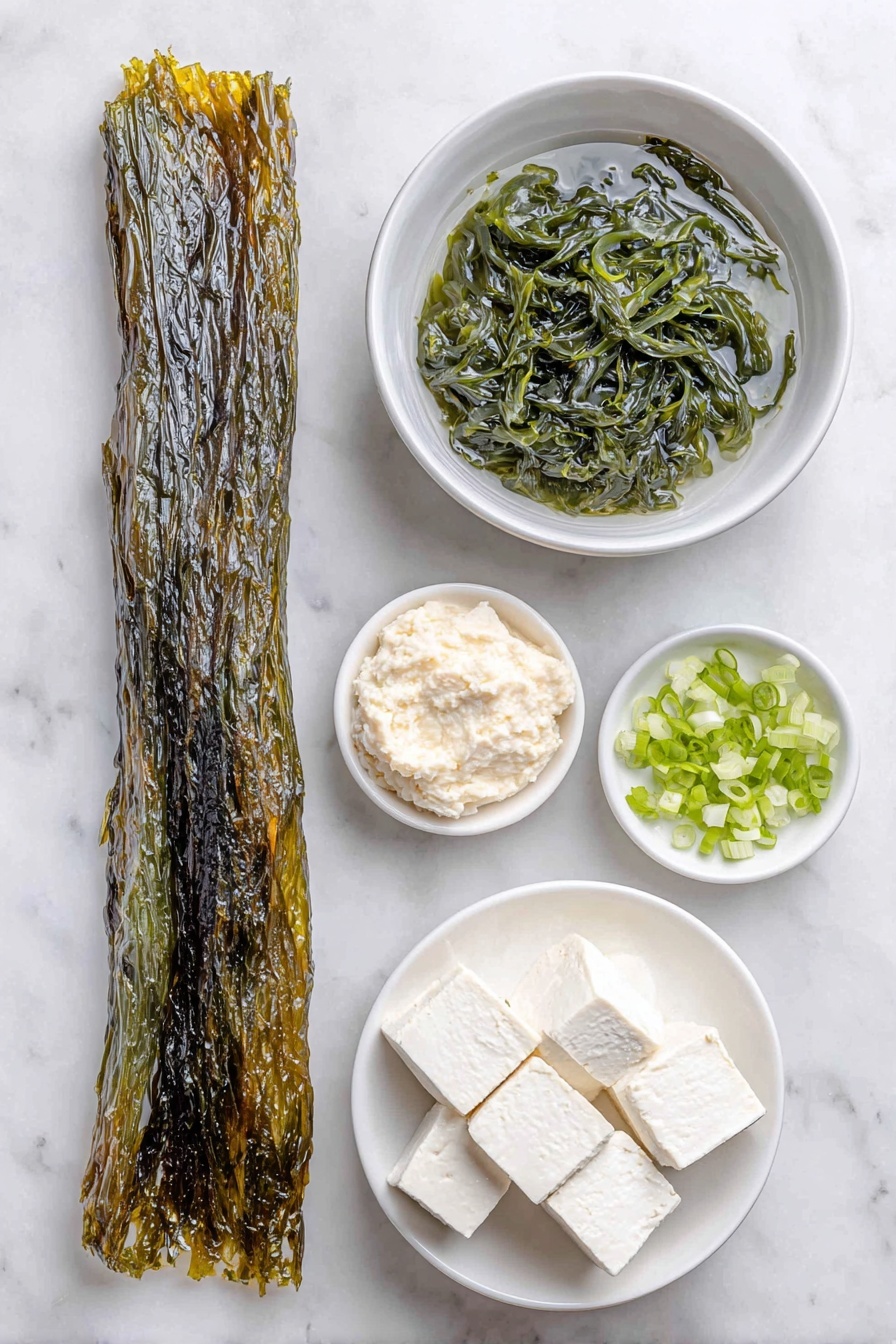 Flat lay of a long dark green fresh kombu seaweed strip, a small white ceramic bowl filled with clear water, a small white ceramic bowl holding rehydrated dark green wakame seaweed, a small white ceramic bowl with smooth pale beige white miso paste, a small pile of freshly chopped bright green onion pieces, a neat arrangement of soft white silken tofu cubes, a small white ceramic bowl filled with dark amber tamari soy sauce, placed on a clean white marble surface, soft natural light, photo taken with an iPhone, professional food photography style, fresh ingredients, white ceramic bowls, no bottles, no duplicates, no utensils, no packaging --ar 2:3 --v 7 --p m7354615311229779997 - Miso Soup with Seaweed and Tofu, Japanese Miso Soup, Healthy Miso Soup, Tofu and Seaweed Soup, Quick Miso Soup