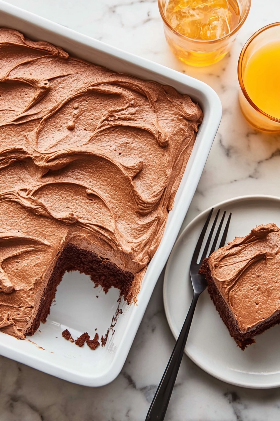 A white rectangular baking dish holds a thick layer of smooth, light brown chocolate frosting spread evenly, with visible swirls and soft peaks on top. One square piece has been removed from the bottom right corner of the dish, showing a dark brown chocolate cake layer beneath the frosting. Next to the dish, on a small white round plate, sits the removed cake piece with the same rich frosting on top, accompanied by a black fork resting beside it. In the top right corner, there is a glass of orange drink on the white marbled surface. Photo taken with an iphone --ar 2:3 --v 7 - Moist Chocolate Mayonnaise Sheet Cake, chocolate mayonnaise cake, easy chocolate sheet cake, homemade chocolate cake, moist chocolate cake recipe