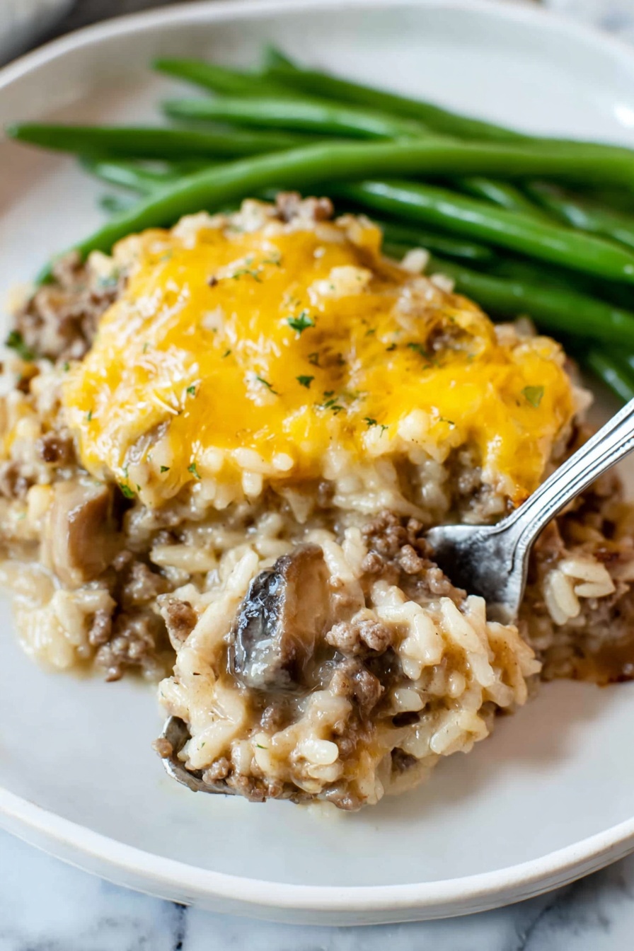 The dish shows two main layers on a white plate with green beans at the back. The bottom layer is a mix of cooked rice, ground meat, and slices of mushrooms, all combined in a creamy sauce with a light brown color and soft texture. The top layer is a covering of melted yellow cheese, unevenly spread, adding a slightly shiny and smooth look. The green beans are long and firm, bright green, placed behind the main dish. A silver fork is lifting a spoonful from the bottom layer, showing the mix of rice, meat, and mushrooms clearly. The plate is set on a white marbled surface photo taken with an iphone --ar 2:3 --v 7 - Cheesy Ground Beef and Rice Casserole, hearty beef and rice bake, easy cheesy casserole, family-friendly comfort food, quick dinner ideas