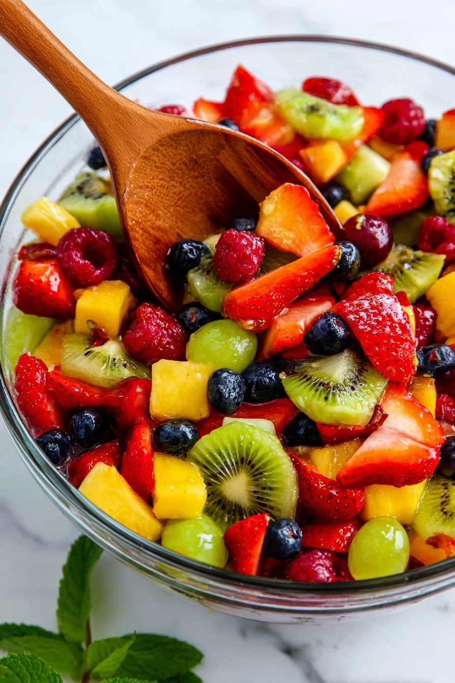 A clear glass bowl filled with colorful mixed fruit salad showing at least six layers of fruit pieces: bright red strawberries sliced and whole, green kiwi slices with black seeds, small dark blue blueberries, red raspberries, yellow pineapple cubes, and green grapes cut in halves. A wooden spoon is resting inside the bowl, scooping some of the fruit, and a sprig of fresh green mint is visible near the bottom right corner. The whole scene is set on a white marbled texture background photo taken with an iphone --ar 2:3 --v 7 - Delicious Fruit Salad with Lemon Glaze, fruit salad recipes, refreshing summer desserts, easy fruit salad ideas, citrus fruit salad