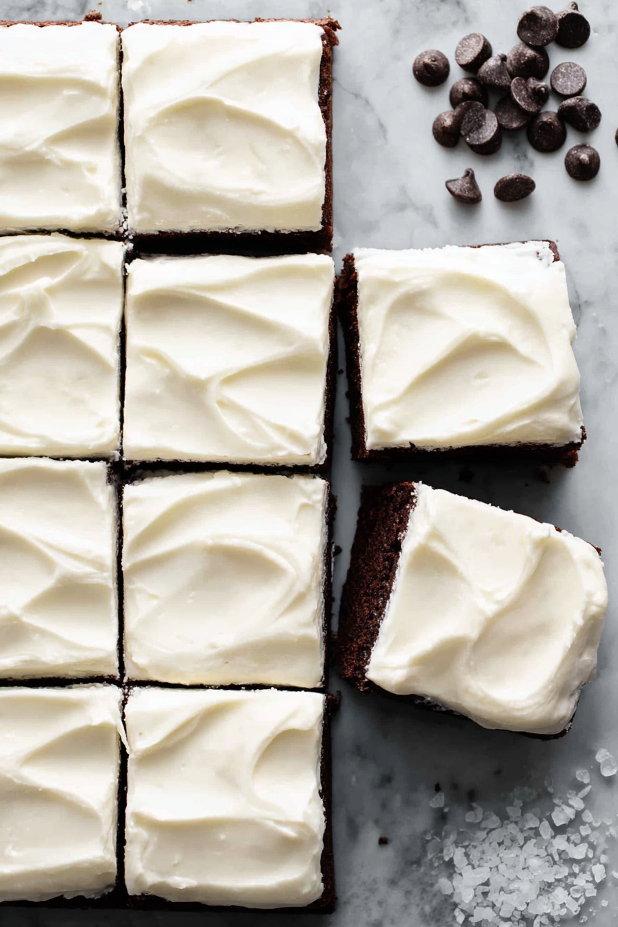 The image shows a dark brown chocolate cake cut into 12 square pieces, nine still together on the left side, and three separated on the white marbled textured surface to the right. Each square has a thick, smooth layer of white cream frosting on top, with gentle swirls creating a soft texture. A few dark chocolate chips are scattered at the top right corner, and some small white salt crystals are near the bottom right edge. The overall look is clean and inviting, with the contrast between the rich dark cake and the bright white frosting clearly visible. photo taken with an iphone --ar 2:3 --v 7 - Baileys Irish Cream Brownies, Irish Cream Brownies, Boozy Chocolate Brownies, Fudgy Bailey's Brownies, Easy Baileys Brownies