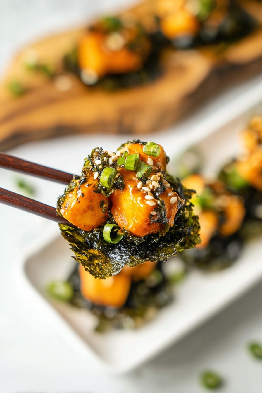 A close-up of a pair of dark brown chopsticks holding a bite-sized stack. The bottom layer is a dark green, wrinkled seaweed sheet, crisp in texture. On top, there are several pieces of light orange cooked cubes with a glossy, slightly creamy bright orange sauce covering them. The stack is garnished with small white sesame seeds and chopped green onions that add green touches to the dish. In the background, a white plate with more similar stacks rests on a white marbled surface. A blurred wooden board with more stacks is visible behind the plate. Photo taken with an iphone --ar 2:3 --v 7 - Baked Salmon Sushi Cups, sushi cups, salmon sushi bites, easy sushi recipes, party finger foods