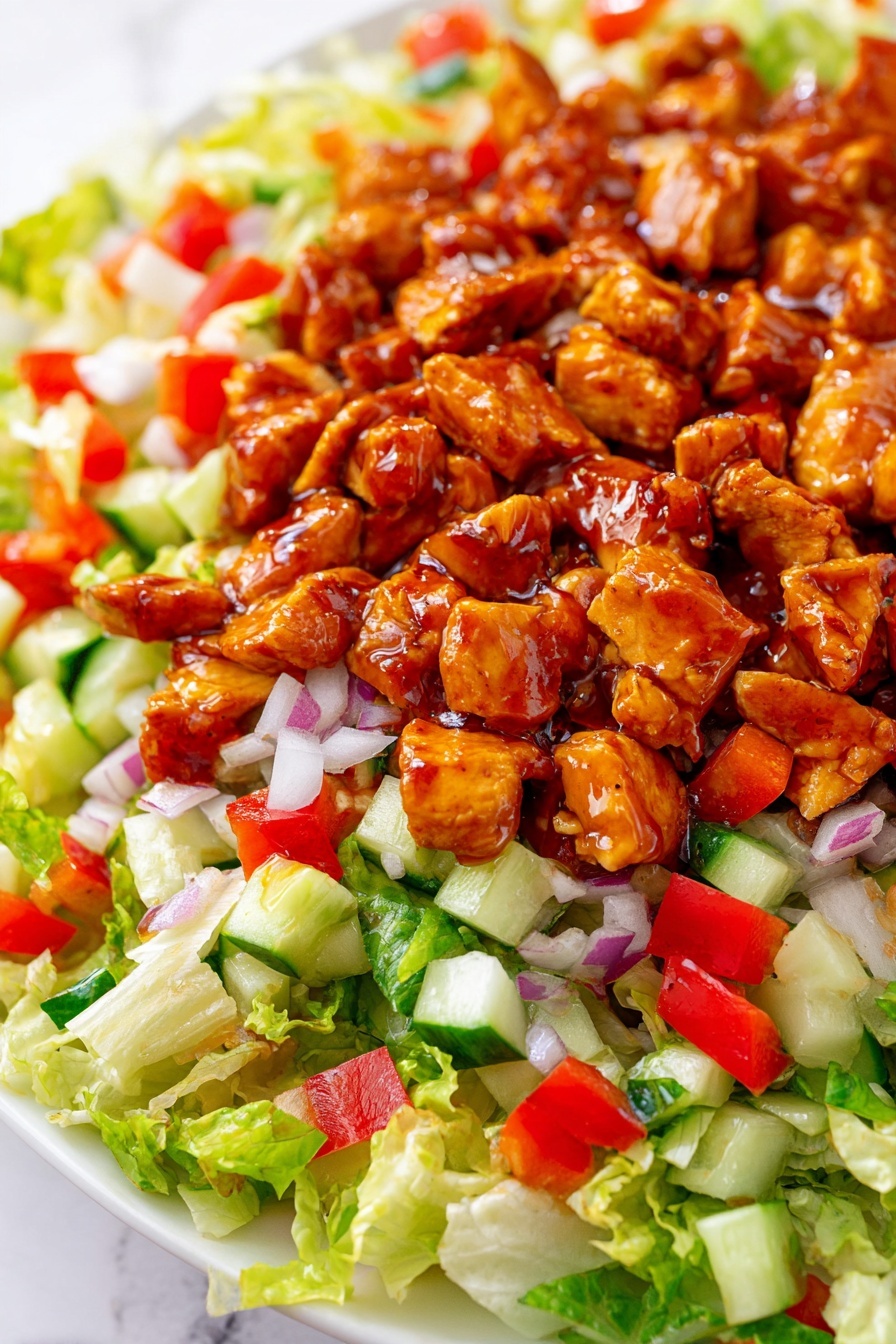 The dish shows a close-up of a salad on a white plate with a white marbled background. The bottom layer has bright green chopped lettuce with a light, crisp texture. Over the lettuce, there are small diced pieces of red bell pepper and white chopped onion spread evenly, adding red and white colors. There are also small cubes of green cucumber scattered throughout this layer. Finally, the top layer consists of chunks of chicken coated in a shiny reddish-brown sauce, giving the salad a rich, glazed look. Photo taken with an iphone --ar 2:3 --v 7 - Honey Hot Chicken Salad, spicy honey chicken salad, easy chicken salad ideas, quick dinner salads, flavorful chicken salad
