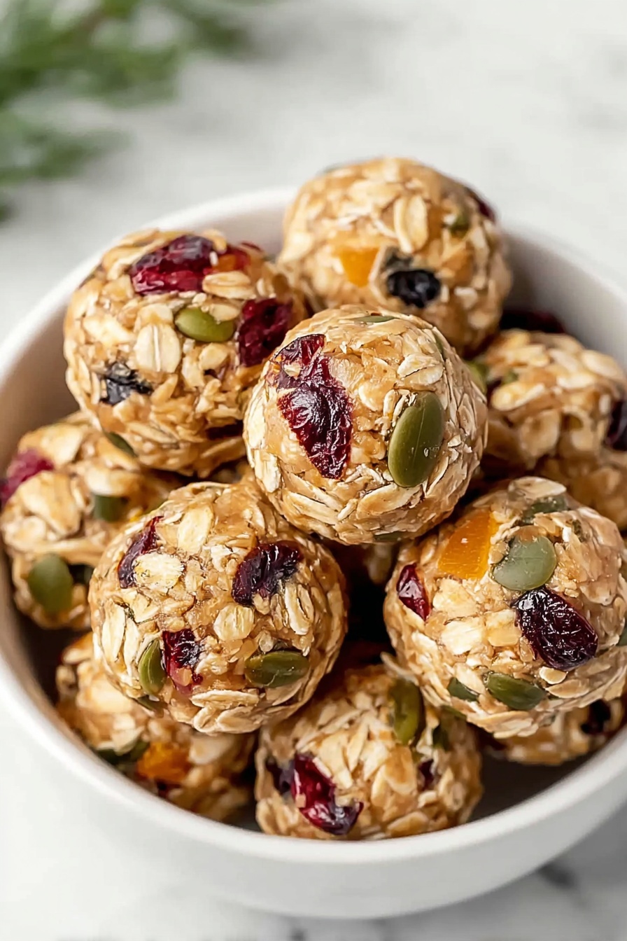 A white bowl filled with round oat energy balls stacked closely together, each ball showing visible layers of light tan rolled oats mixed with bits of dark red dried cranberries, orange pieces, and green pumpkin seeds scattered throughout. The texture looks chewy and dense with the seeds and fruit pieces pressed into the smooth dough. The bowl sits on a white marbled surface with a hint of green plant leaves blurred in the background. The focus is sharp on the oats and seeds, highlighting their natural colors and textures. Photo taken with an iphone --ar 2:3 --v 7 - Pumpkin Seed Cranberry Energy Balls, healthy energy bites, nutritious snack recipes, easy no-bake energy snacks, vegan berry snack ideas